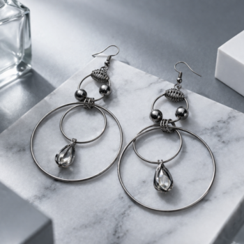 Stylish gunmetal drop earrings with crystal pendant on marble background, modern jewelry