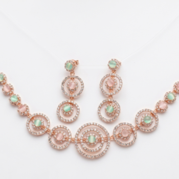 Rose gold circular necklace set with pastel green and blush stones displayed on velvet background with matching earrings
