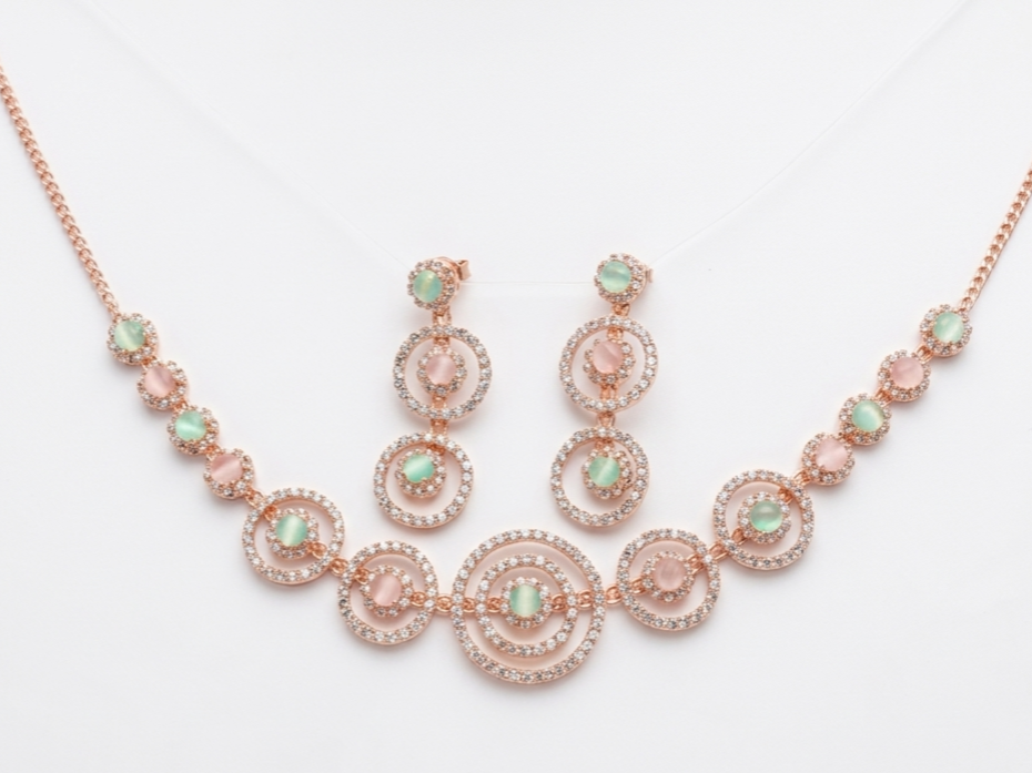 Rose gold circular necklace set with pastel green and blush stones displayed on velvet background with matching earrings