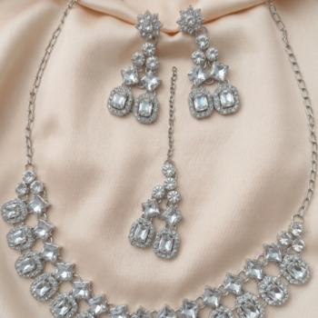 Silver crystal necklace set with oval and geometric stones displayed on soft fabric with matching earrings and maang tikka