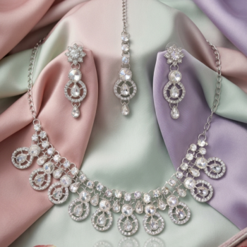 Silver crystal necklace set with teardrop stones displayed on pastel fabric with earrings and maang tikka